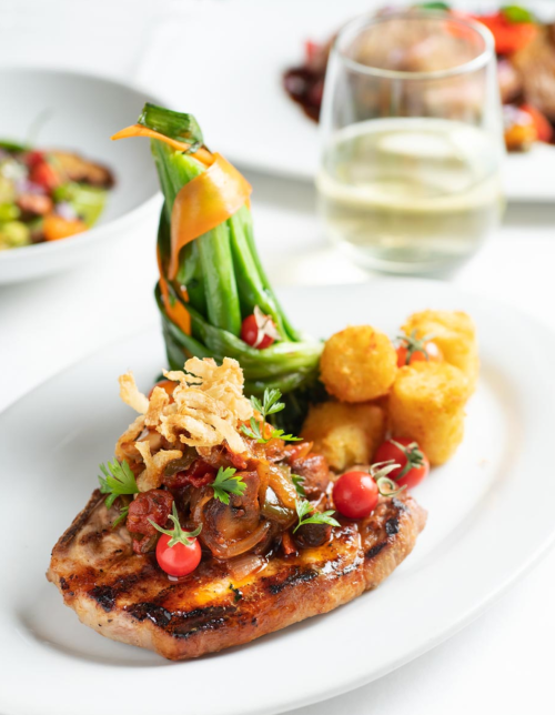 Grilled chicken with tomato sauce, crispy onions, green beans, and a glass of white wine on a white plate.